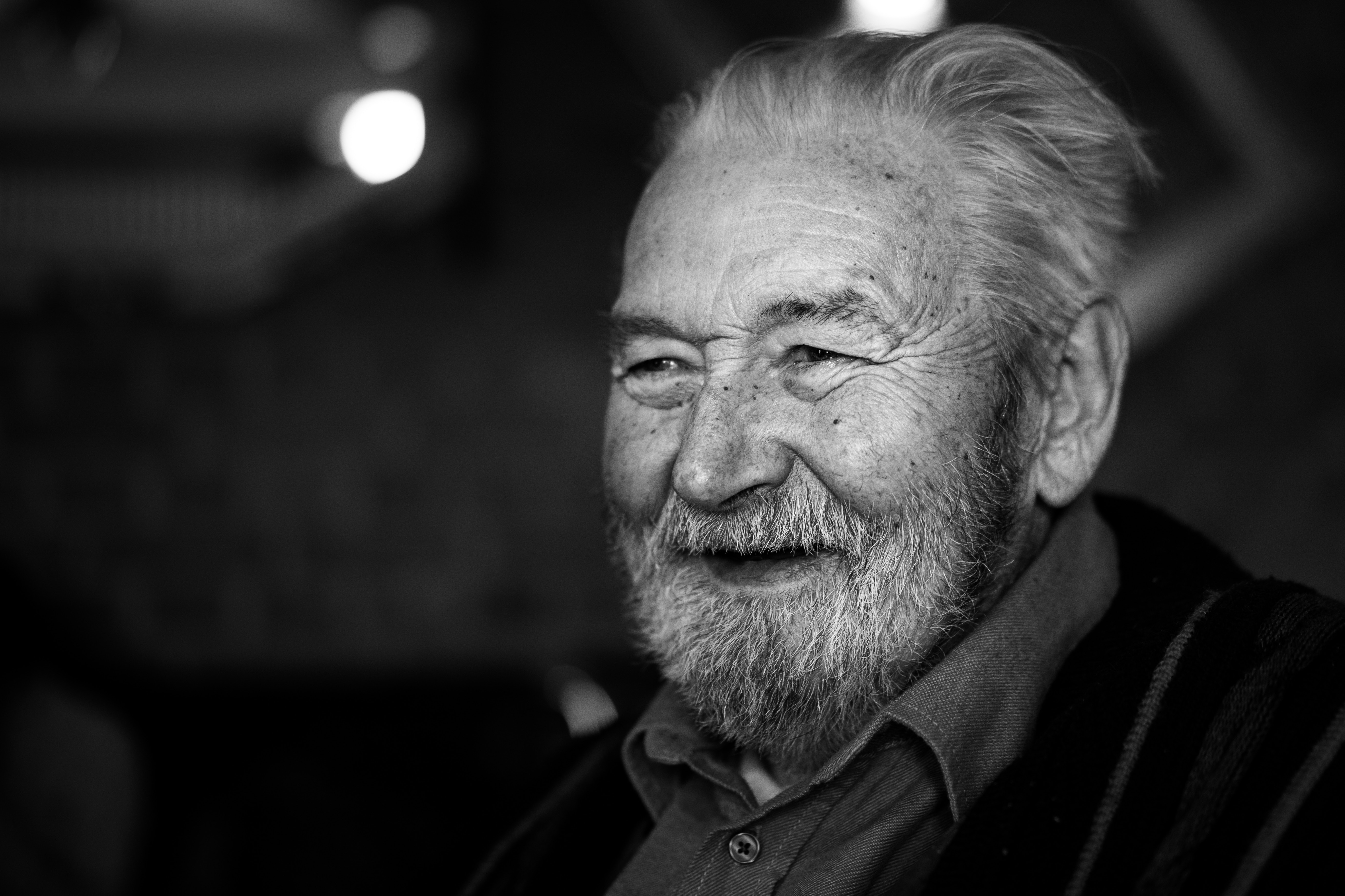 black and white image facial of an old smiling man with beard glimmer in eyes