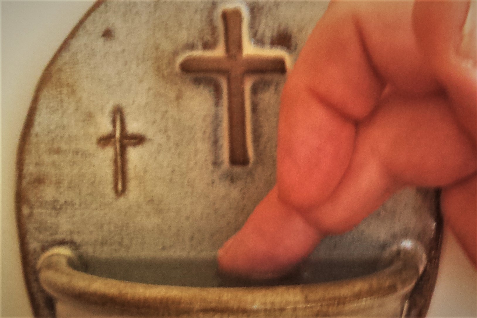 holy water font with water and a cross.  person's fingers dipping in the water,