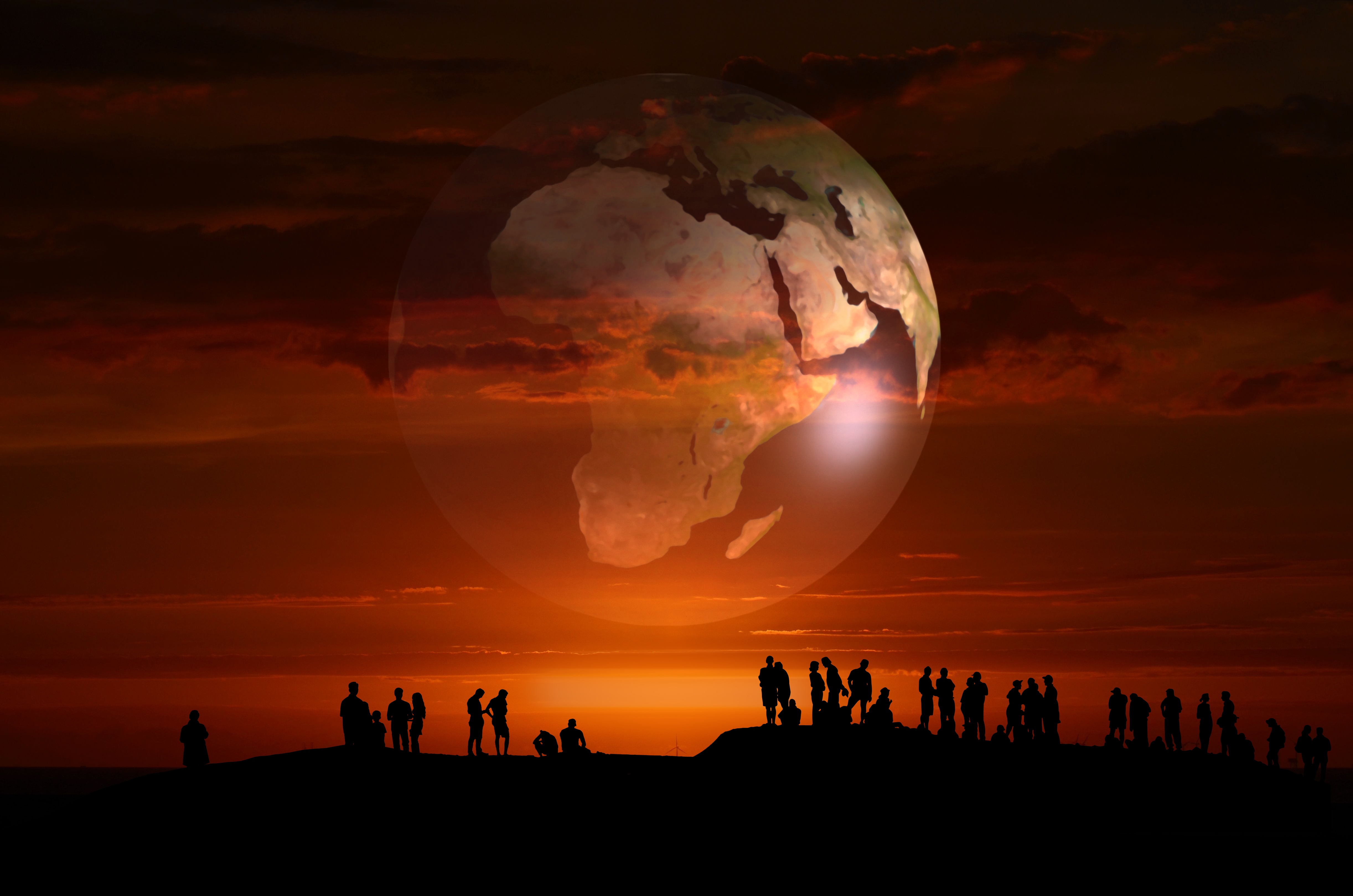 image of world matted on an orange sunrise silhouette of people of cliff at bottom of image